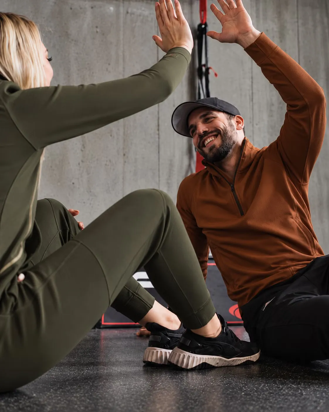 Duas pessoas sentadas no chão da academia batendo as mãos em comemoração